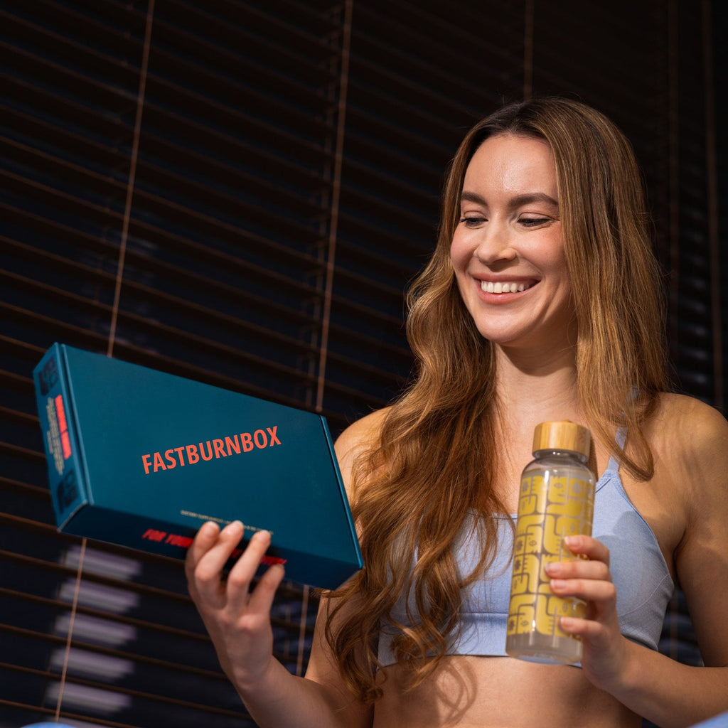 Smiling woman holding a FastBurnBox kit box and a patterned glass water bottle